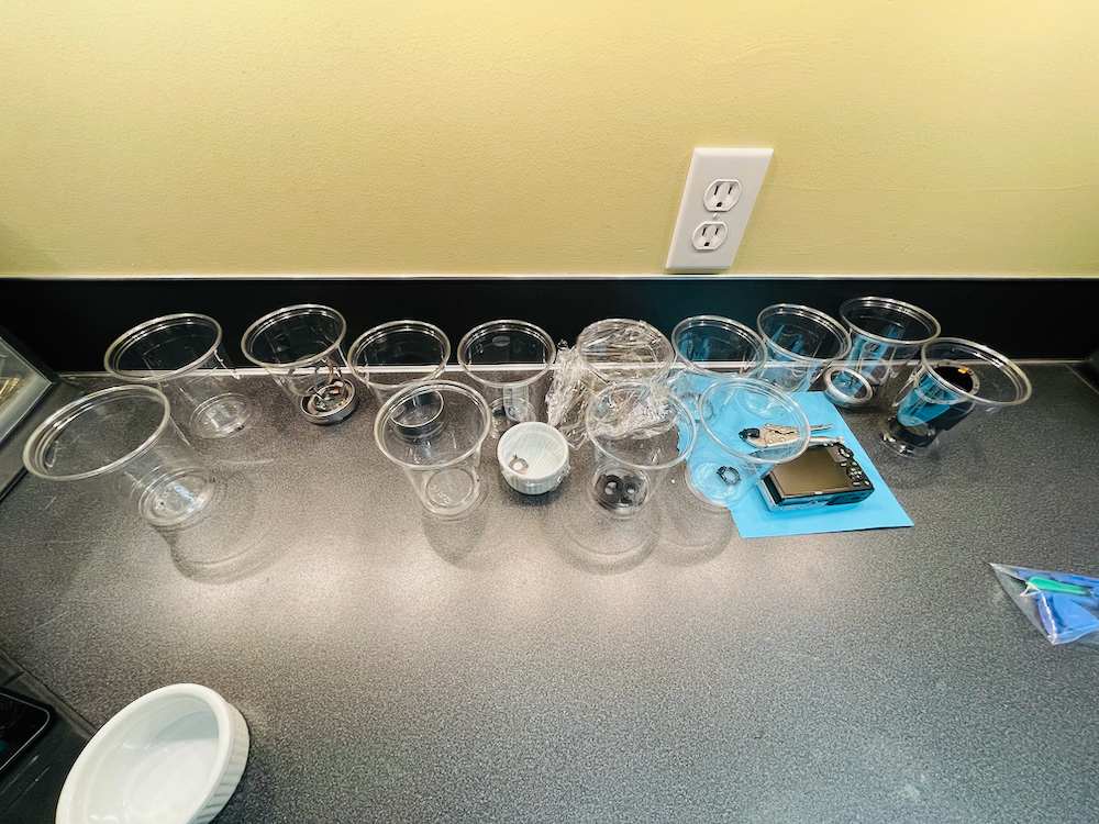 approximately 16 cups on workbench containing camera parts